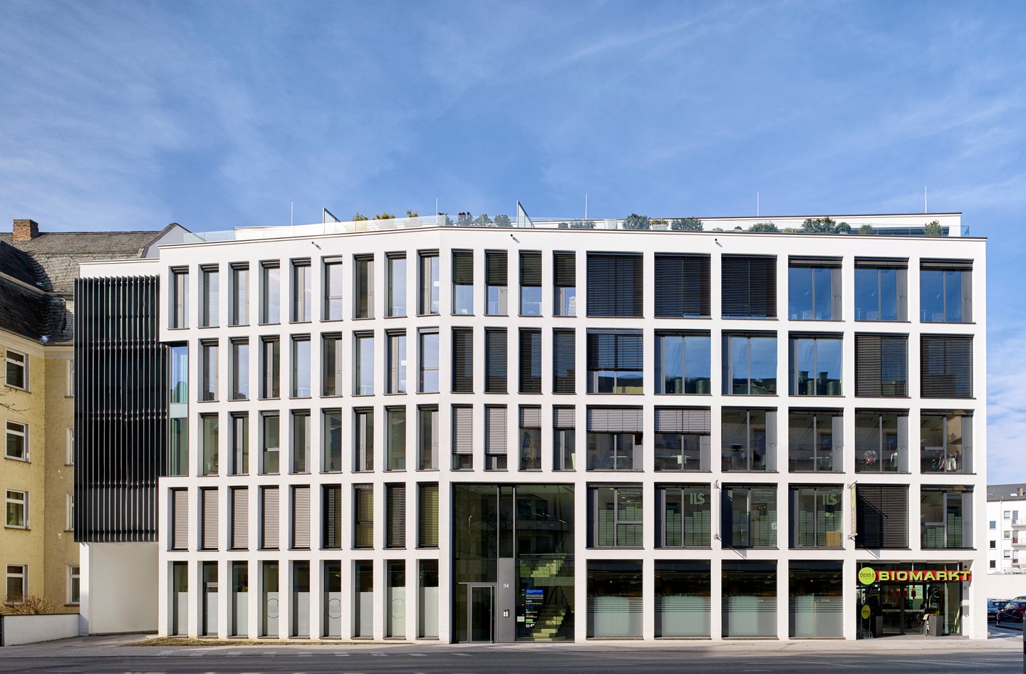 Gesamtansicht des Hauses mit heller Lochfassade und gläsernem Erdgeschoss.
