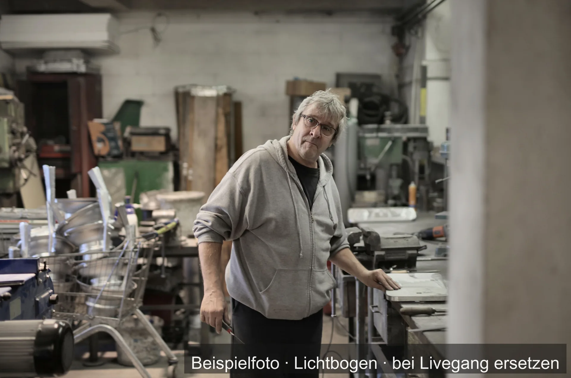 Ein Mann mit Brille steht an der Werkbank einer Metallwerkstatt.