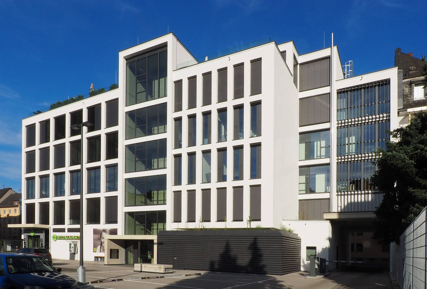 Helles Wohn-, Büro- und Geschäftshaus mit Lochfassade, Glasfeldern in Pfosten-Riegel-Bauweise und gläsernem Erdgeschoss.